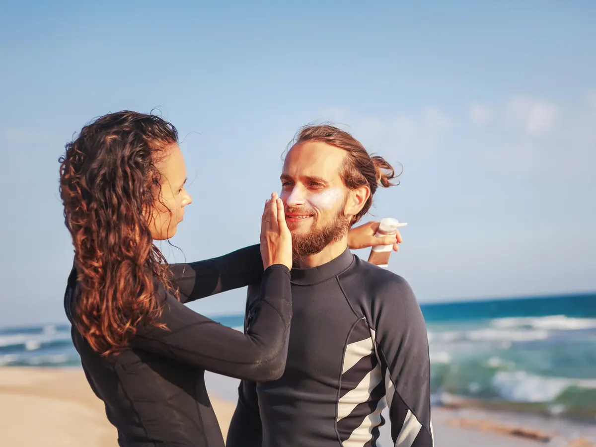 Two surfers on a beach applying sun protection to the face