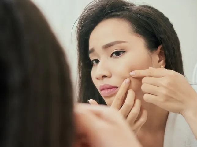 Woman examining a blemish on her cheek in a mirror