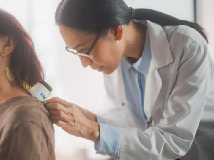 Dermatologist examining an older woman's neck with a handheld device