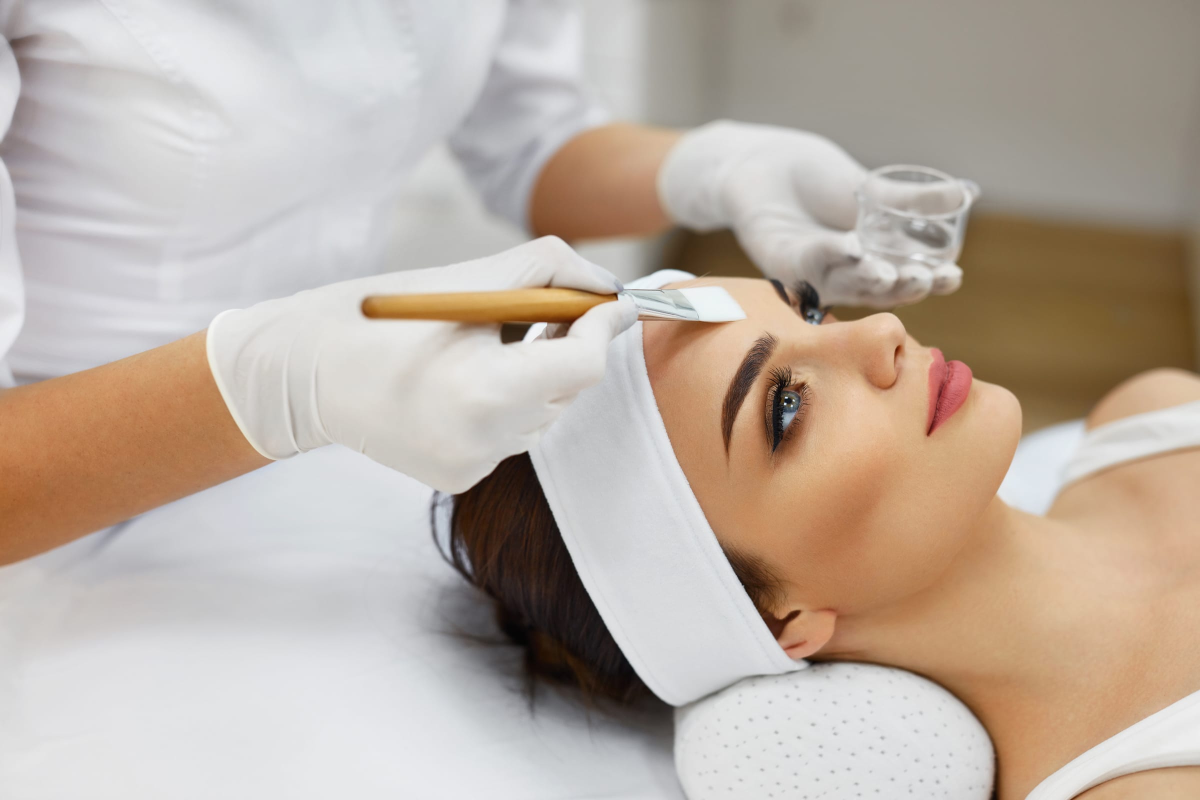 Cosmetician gently applying hydrating product to a relaxed woman's face in a bright spa treatment room
