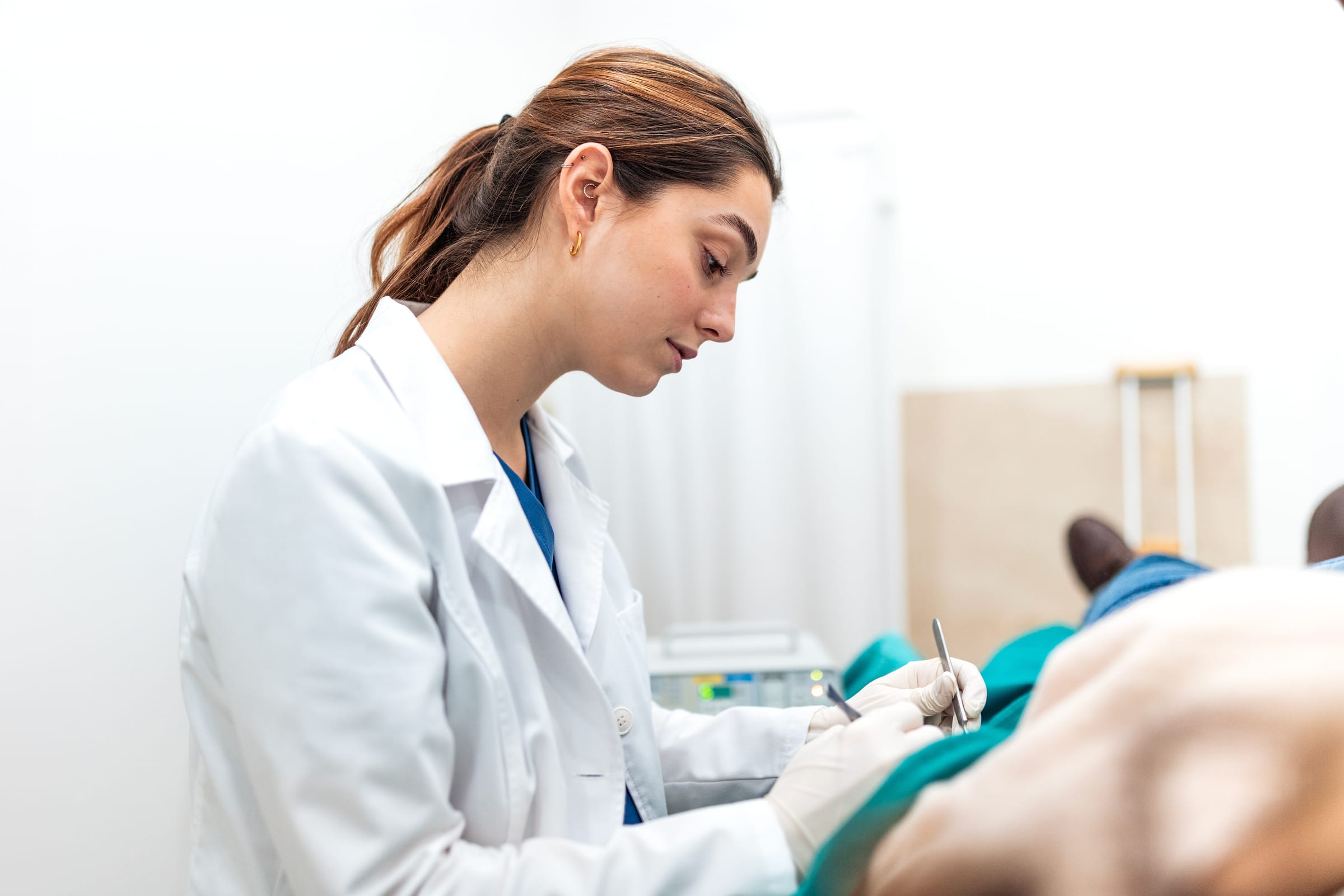 Doctor in a white coat using fine instruments during a minor procedure on a patient under a green surgical drape