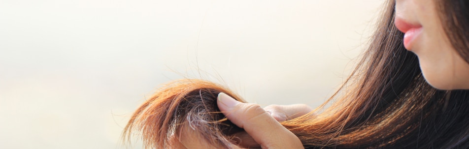 Woman holding a strand of her hair up to look at it