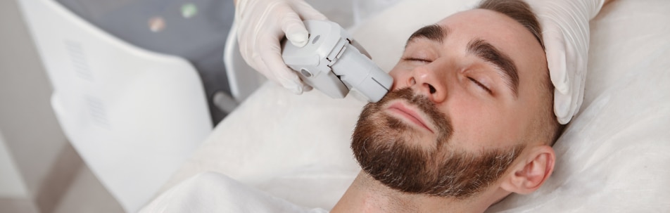 Man lying back while a gloved clinician holds a laser handpiece to his cheek