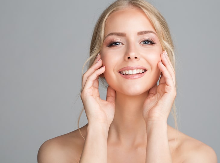 Smiling woman with blonde hair resting her hands on her face in a studio portrait