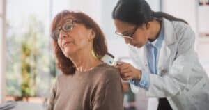 Dermatologist examining an older woman's neck with a handheld device
