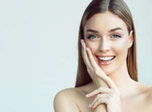 Woman touching her face smiling with clear, healthy skin from wart or mole removal in Los Angeles, CA