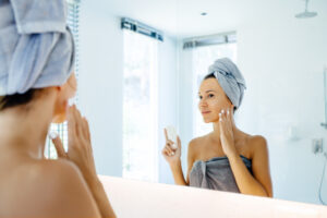 Woman looking in the mirror applying moisturizer for Eczema on the face in Los Angeles, CA